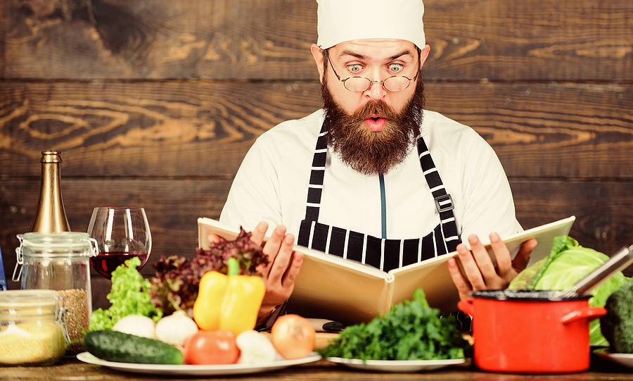 Culinary arts. Recipe to cook healthy food. Vegetarian recipe. Experienced chef cooking excellent dish. This recipe is just perfect. Man bearded hipster read book recipe near table fresh vegetables